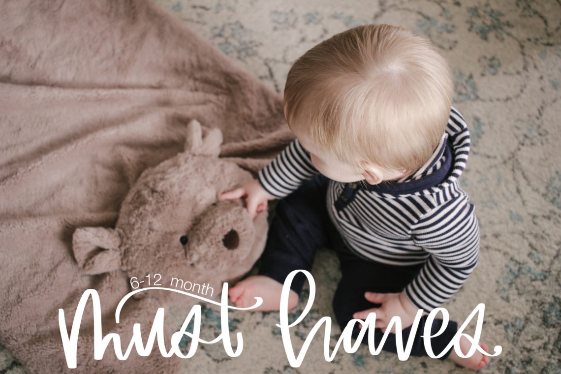 Photo of an 8-month old infant with a bear playmat, with white text reading "6-12 Month Must-Haves"