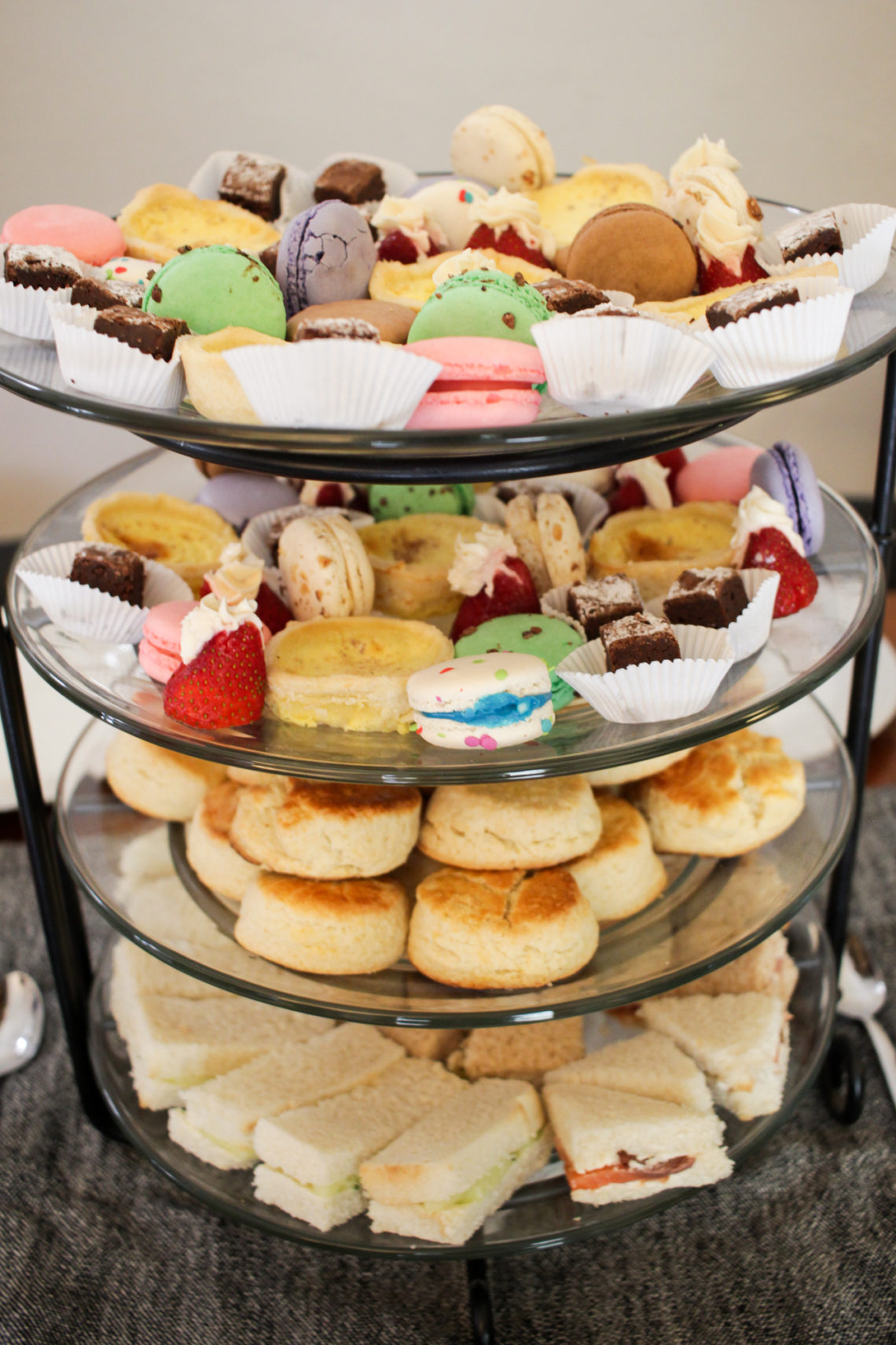 How to host the perfect afternoon tea: Image of a 4-tiered server with sandwiches, scones, and desserts.